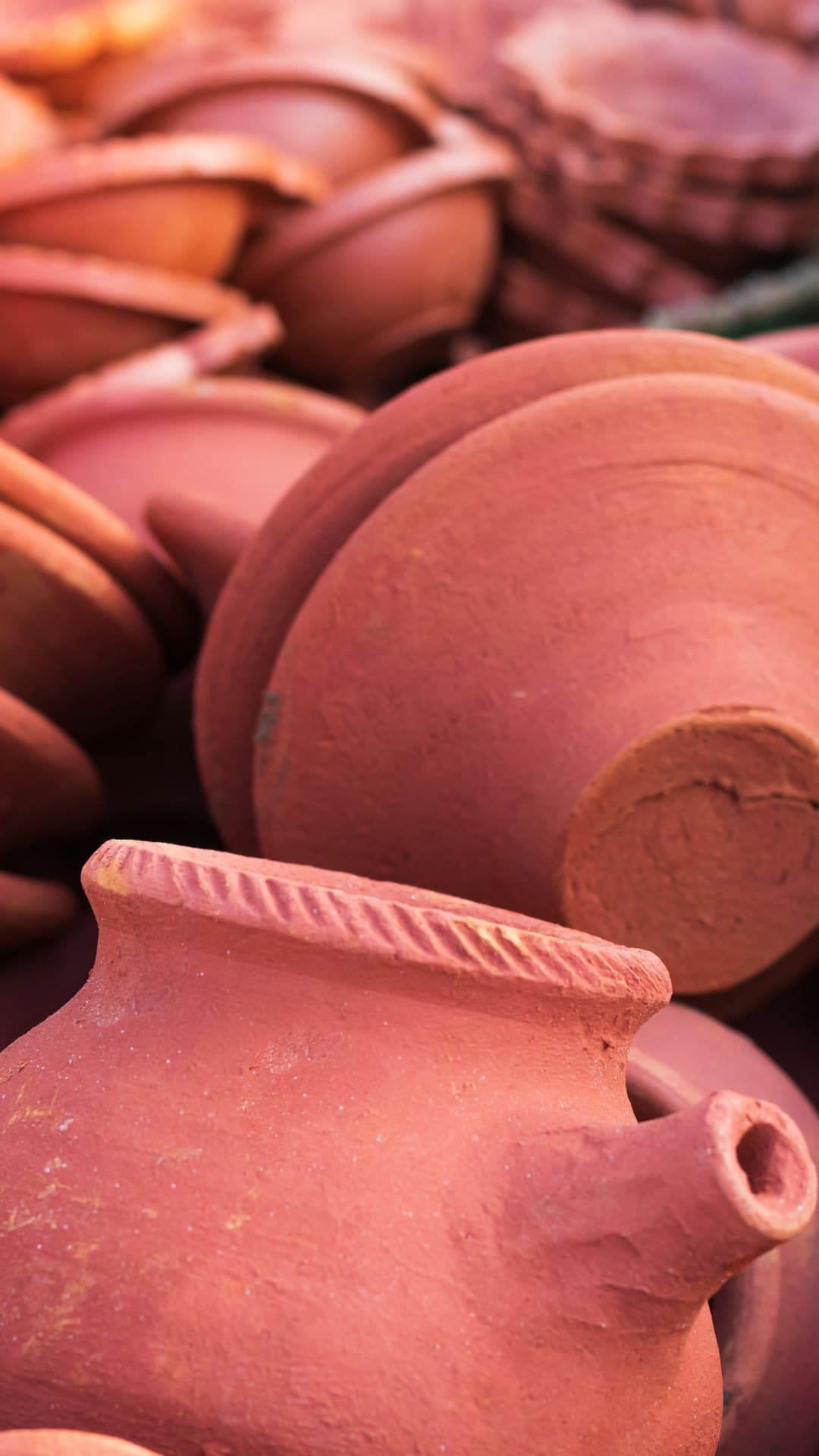 Locally made earthenware pots and bowls stacked for sale at market.